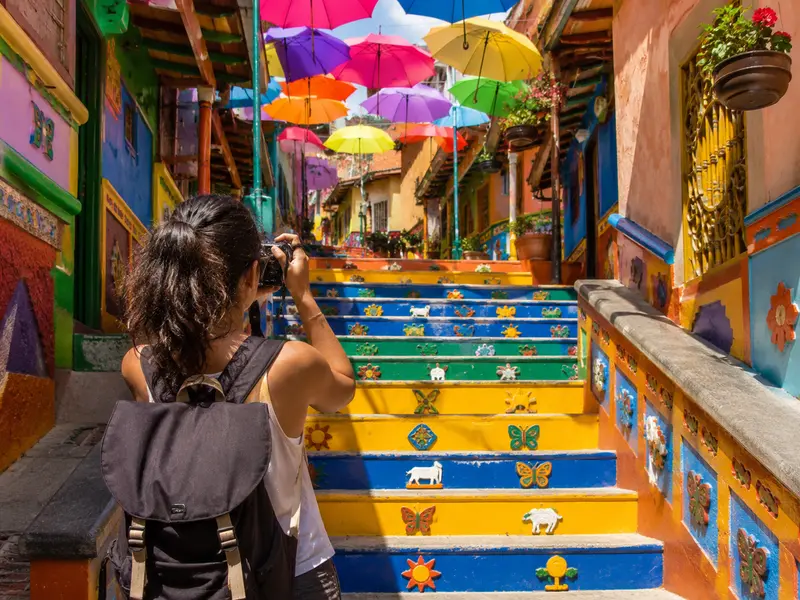 Traveler photographing the colorful umbrella-covered zócalo stairs in Guatapé