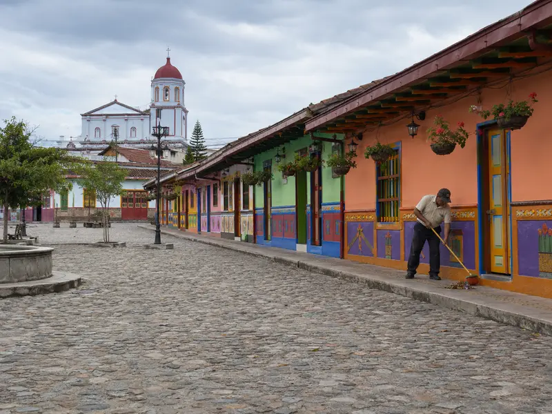 Quiet Guatapé plaza on a weekday morning with a local sweeping in front of colorful facades